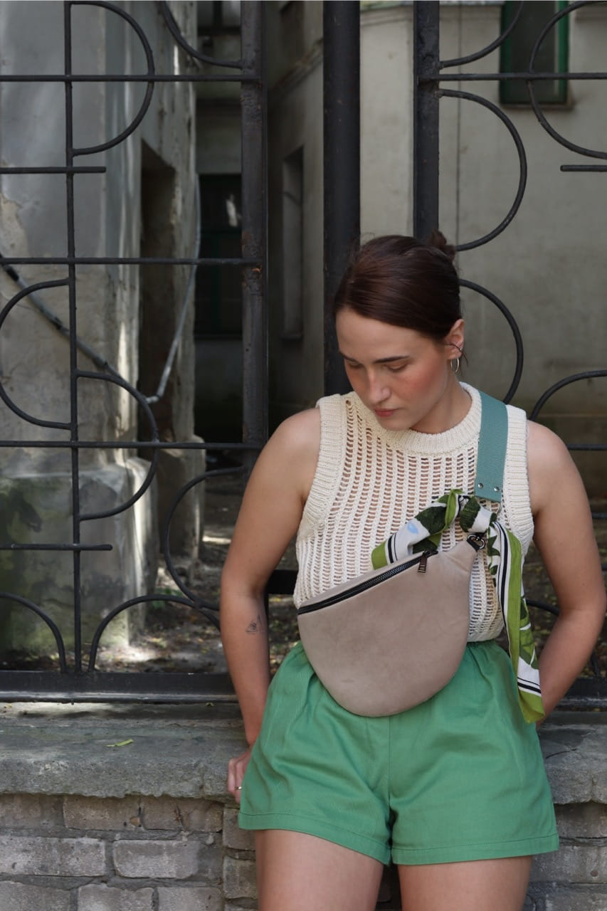 Jasnobeżowa nerka Oxford Tan. Trwały aksamit. Okucia w starym srebrze. Prezentowana przez modelkę w rozmiarze midi, z paskiem z taśmy 40mm w kolorze szara mięta.