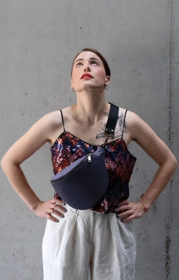 Lawendowa nerka aksamitna Heron. Trwały materiał. Okucia w starym złocie. Modelka prezentuje rozmiar midi, na pasku z czarnej taśmy 40mm.