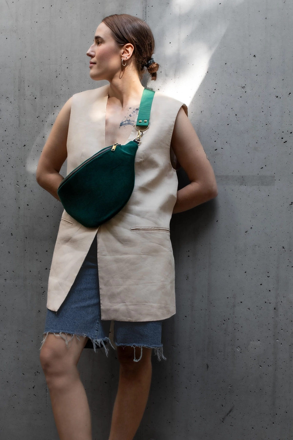 Aksamitna nerka Ponderosa Green, w rozmiarze maxi z paskiem z ciemnozielonej taśmy 40 mm. Prezentowana na modelce wraz z beżową kamizelką i dżinsowymi bermudami.